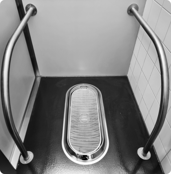 Missoir Hockurinal mit Haltestangen aus Edelstahl, eingebaut in einer öffentlichen Toilettenkabine